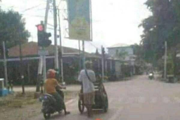 Seorang pria di Malaka dengan gerobak dorong ikut berhenti bersama seorang pengendara kendaraan roda dua, saat lampu lalu lintas menunjukkan tanda merah. 